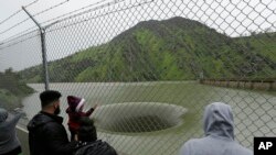 People stop to watch water flow into the iconic Glory Hole spillway at the Monticello Dam, Feb. 20, 2017, in Lake Berryessa, Calif. Water is flowing for the first time in over a decade into the 72-foot diameter hole due to the recent storms in California.