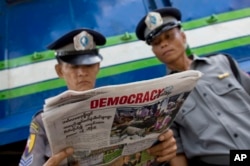 Police officers read a copy of the newspaper "Democracy Today" in Yangon, Myanmar, Wednesday, Nov. 11, 2015.