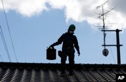 FILE - A worker wearing cleans radiation-exposed roof tiles at a private house in Minamisoma, Fukushima prefecture, northeastern Japan, Feb. 24, 2016. About 7,000 day laborers are cleaning up this irradiated town north of the Fukushima nuclear plant.