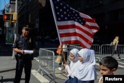 Anak-anak membawa bendera Amerika melewati petugas kepolisian New York dalam pawai tahunan Hari Muslim di New York, 24 September 2017. (Foto: REUTERS/Stephanie Keith)