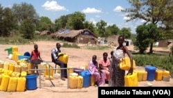A woman refugee waits to add her jerry cans to the long line at a watering hole in a Uganda refugee settlement housing thousands of South Sudanese.