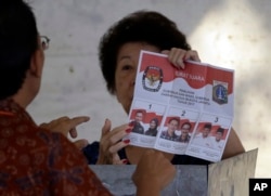 FILE - An election official explains to an elderly woman how to give her vote at a polling station in Jakarta, Feb. 15, 2017.