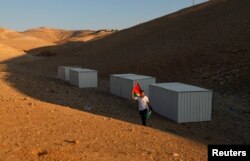 A man holds a Palestinian flag as he walks near shacks installed by activists to protest the Israeli plan to demolish the Bedouin village of Khan al-Ahmar, in Khan al-Ahmar, occupied West Bank, Sept. 11, 2018.