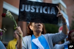 A woman holds up a sign that reads in Spanish "Justice" as she gathers with others outside the funeral home where a private wake is held for prosecutor Alberto Nisman in Buenos Aires, Jan. 29, 2015.