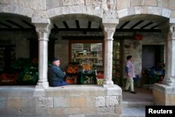 FILE - An old man rests under the medieval arches in the old city of Besalu, near Girona, in the northeastern region of Catalonia, Spain, April 5, 2014.