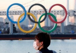 Seorang pria mengenakan masker di tengah pandemi COVID-19 di depan lambang cincin Olimpiade raksasa di Tokyo, Jepang, 13 Januari 2021. (Foto: dok)