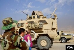 Local Christians and Kurdish peshmerga fighters watch as Iraqi armor trundles past them, in Bartilla, Iraq, Oct. 31, 2016. (J. Dettmer/VOA)