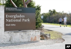 Visitors walk past a sign for Everglades National Park as they enter from overflow parking, Jan. 2, 2019, in Everglades National Park, Fla. Human feces, overflowing garbage, illegal off-roading and other damaging behavior in fragile areas were beginning to overwhelm some of the West's iconic national parks, as a partial government shutdown left the areas open to visitors but with little staff on duty.