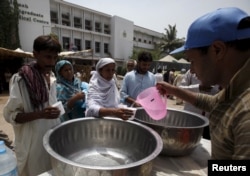 Warga menerima air minum yang dibagikan di Jinnah Postgraduate Medical Center (JPMC) di Karachi, Pakistan (23/6).