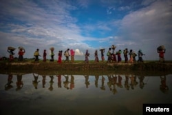FILE - Rohingya refugees are reflected in rainwater along an embankment next to paddy fields after fleeing from Myanmar into Palang Khali, near Cox's Bazar, Bangladesh, Nov. 2, 2017.
