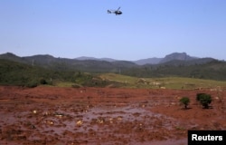 FILE - A helicopter flies over the Bento Rodrigues district, covered with mud after a dam owned by Vale SA and BHP Billiton Ltd burst in Mariana, Brazil, Nov. 6, 2015.