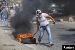 A Palestinian protester drags a burning tyre during clashes with Israeli troops in the West Bank city of Hebron, Oct. 18, 2015.