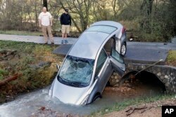 Tanager Tyler and his son Mitchell look over a vehicle that wound up in the culvert under their driveway after floodwaters swept it and its four occupants off the road during the previous night in Pinson, Ala., Dec. 26, 2015.