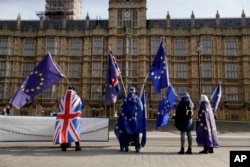 FILE - Pro-EU membership supporters hold European Union flags as they protest against Brexit across the street from the Houses of Parliament in London, Tuesday, Jan. 30, 2018.