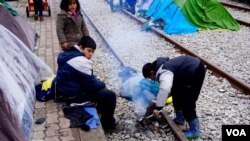 Children along tracks that lead to Macedonian boarder attempt to light fire to stay warm, in Idomeni, Greece, March 16, 2016. (J. Dettmer/VOA)
