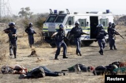 FILE - A policeman gestures in front miners after they were shot dead outside a South African mine in Rustenburg, 100 km (62 miles) northwest of Johannesburg, Aug. 16, 2012.
