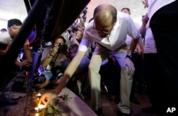 Former Philippine President Benigno Aquino III places a candle under a picture of victims of alleged extrajudicial killings after a mass at the University of the Philippines Church of the Holy Sacrifice.