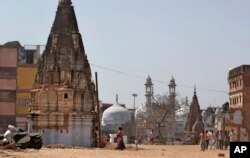 The 17th-century Gyanvapi mosque, the white structure sandwiched between Hindu temples, is seen in the background, March 19, 2019, as Hindu devotees walk at the site of a proposed grand promenade connecting the sacred Ganges river with a centuries-old temple dedicated to Lord Shiva, in Varanasi, India.