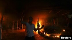 A protester reacts as the U.S. Consulate in Benghazi is seen in flames during a protest by an armed group said to have been protesting a film being produced in the United States September 11, 2012.