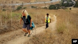In this July 25, 2019, photo, Beth Pratt, California director for the National Wildlife Federation, left, and Cal Trans project manager Sheik Moinuddin walk along a hiking trail near a proposed wildlife crossing over U.S. Highway 101, background, in Agour