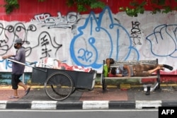Seorang pemulung menarik gerobak sementara seorang pria tertidur di kursi, Jakarta, 21 April 2020. (Foto: AFP)
