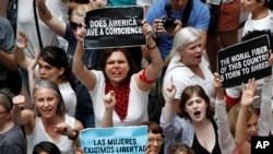 Women hold signs as they protest the separation of immigrant families, June 28, 2018, inside the Hart Senate Office Building on Capitol Hill in Washington.