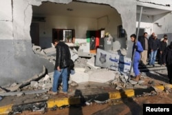 FILE - Civilians and security personnel stand at the scene of an explosion at a police station in Tripoli, Libya, a blast later claimed by militants professing loyalty to Islamic State, March 12, 2015.