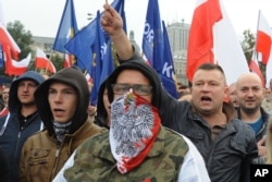 FILE - Protesters shout anti-migrant slogans as several thousand right-wing nationalists rally, demonstrating against EU proposed quotas for Poland to spread the human tide of refugees around Europe, in Warsaw, Poland, Sept. 12, 2015.