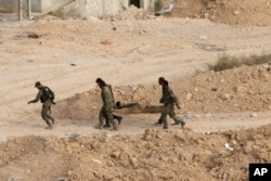 FILE - Syrian soldiers carry a wounded comrade on a stretcher in Harasta, northeast of Damascus, Syria, Oct. 22, 2015.
