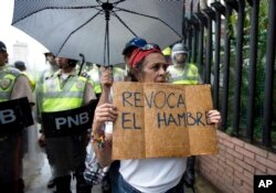 FILE - In this July 27, 2016, file photo, a woman holds a sign with a message that in reads in Spanish "Revoke hunger" during a protest march in Caracas, Venezuela.
