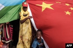 FILE - People hold Chinese and Djiboutian national flags as they wait for the arrival of Djibouti’s president, Ismaïl Omar Guelleh, before the launching ceremony of a China-financed 1,000-unit housing construction project in Djibouti, July 4, 2018.
