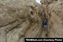 National parks traveler Mikah Meyer navigates his way through naturally-formed passageways that lead to a stone shelf overlooking the ancient structures at Chaco Culture National Historical Park.