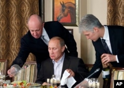 FILE - Businessman Yevgeny Prigozhin, left, serves food to Russian Prime Minister Vladimir Putin, center, during dinner at Prigozhin's restaurant outside Moscow, Russia, Nov. 11, 2011.