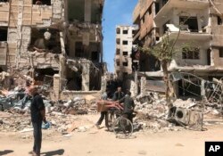 People stand in front of damaged buildings, in the town of Douma, the site of a suspected chemical weapons attack, near Damascus, Syria, April 16, 2018.