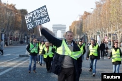FILE - A man wearing a yellow vest, a symbol of French drivers' protest against higher fuel prices, holds a placard with the message, "World Champions in Taxes", as demonstrators gather on the Champs Elysees in Paris, France, Nov. 17, 2018.