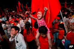 A child joins adult supporters of Myanmar's National League for Democracy party to celebrate as unofficial election results are posted outside the NLD headquarters in Yangon, Myanmar, Nov. 9, 2015.