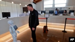 In this photo dated March 12, 2018, Mihail Slanina, a guest from Moldavia, asks robot Robby Pepper for information at the front desk of hotel in Peschiera del Garda, northern Italy. The hotel uses the robot to assist guests. (AP Photo/Luca Bruno)