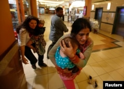 FILE - Women carrying children run for safety as armed police hunt for gunmen who went on a shooting spree in Westgate shopping center in Nairobi, Kenya, Sept. 21, 2013.