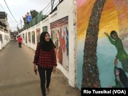 Mila Herliani, ibu rumah tangga yang tinggal di daerah itu, nampak menikmati karya yang dipajang Jitno Slamet di kawasan Cicendo, Bandung, Kamis, 23 Agustus 2018. (Foto: Rio Tuasikal/VOA)