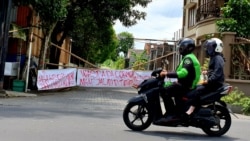 Ojek online melintas di gerbang kampung yang ditutup. Covid-19 berdampak besar pengemudi ojol. (Foto: VOA/Nurhadi)