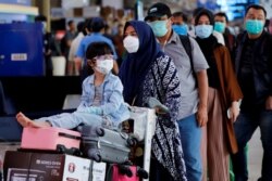 Seorang anak perempuan mengenakan masker bersama ibunya antre untuk pemeriksaan suhu tubuh di tengah penyebaran virus corona (Covid-19) di Bandara Halim Perdanakusuma, Jakarta, 20 Maret 2020. (Foto: Reuters)