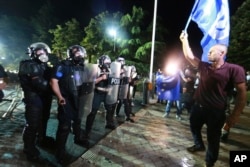 A demonstrator walks past Albanian policemen in riot gear during an anti-government protest in Tirana, Albania, June 8, 2019.