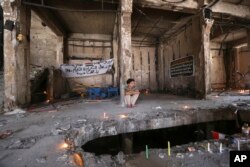 FILE - A man sits amid a makeshift memorial inside a burned mall at the scene of a massive truck bombing last Sunday that killed at least 186 people and was claimed by the Islamic State group, in the Karada neighborhood of Baghdad, Iraq, July 10, 2016.