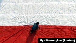 Seorang pria mempersiapkan bendera raksasa sebelum mengibarkannya pada perayaan hari kemerdekaan di Universitas Kristen Petra di Surabaya, Jawa Timur. (Foto: REUTERS/Sigit Pamungkas)