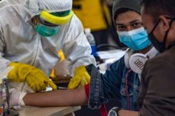 Para petugas kesehatan melakukan pemeriksaan kesehatan 156 pekerja migran Indonesia yang tiba dari Malaysia di Bandara Juanda, Surabaya, 7 April 2020. (Foto: AFP)