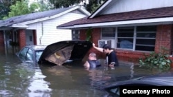 FILE - Andrew Saldivar, left, removes a car battery given to him by a neighbor, which he later installed on a boat to save Houstonians still stranded by the floods. (Photo courtesy of Andrew Saldivar)