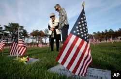 Madeline Fucile, 96, of Centerville, Mass., left, visits the grave of her husband World War II U.S. Navy veteran Dominic Fucile, accompanied by her friend Beverly Donheiser, of Cotuit, Mass., right, in Massachusetts National Cemetery in Bourne, Mass.
