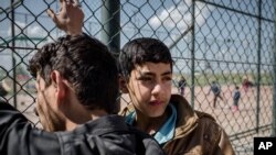 Young men stand next to a fence at a holding center for newly displaced persons from the Iraqi army's offensive against the Islamic State group outside Mahkmour, Iraq, March 31, 2016.
