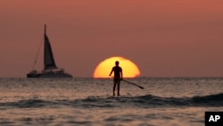 A paddle boarder looks out over the Pacific Ocean as the sun sets off of Waikiki Beach, in Honolulu