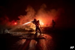 A firefighter sprays the smoldering remains of a vehicle on Interstate 5 as the Delta Fire burns in the Shasta-Trinity National Forest, Calif., on Sept. 5, 2018.
